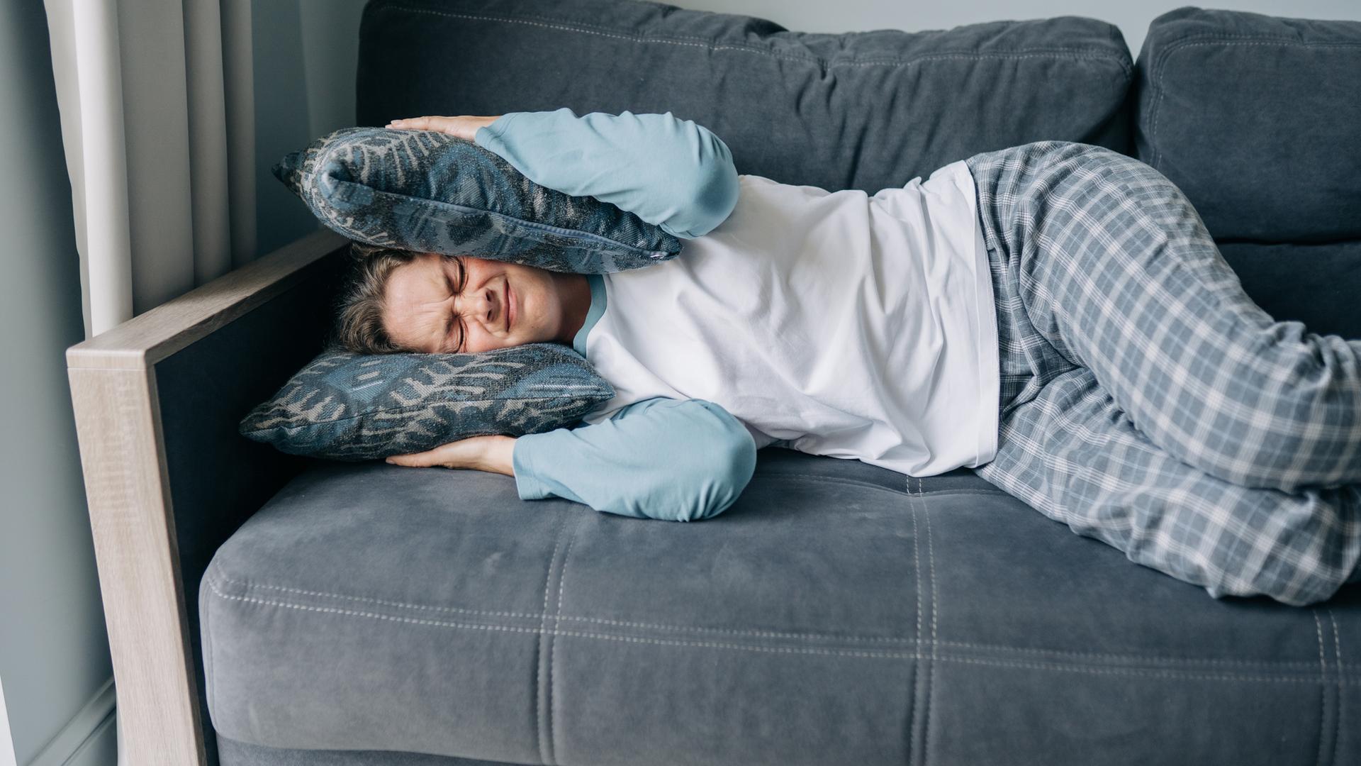 Gestresste Frau hält sich die Ohren mit Kissen zu. 