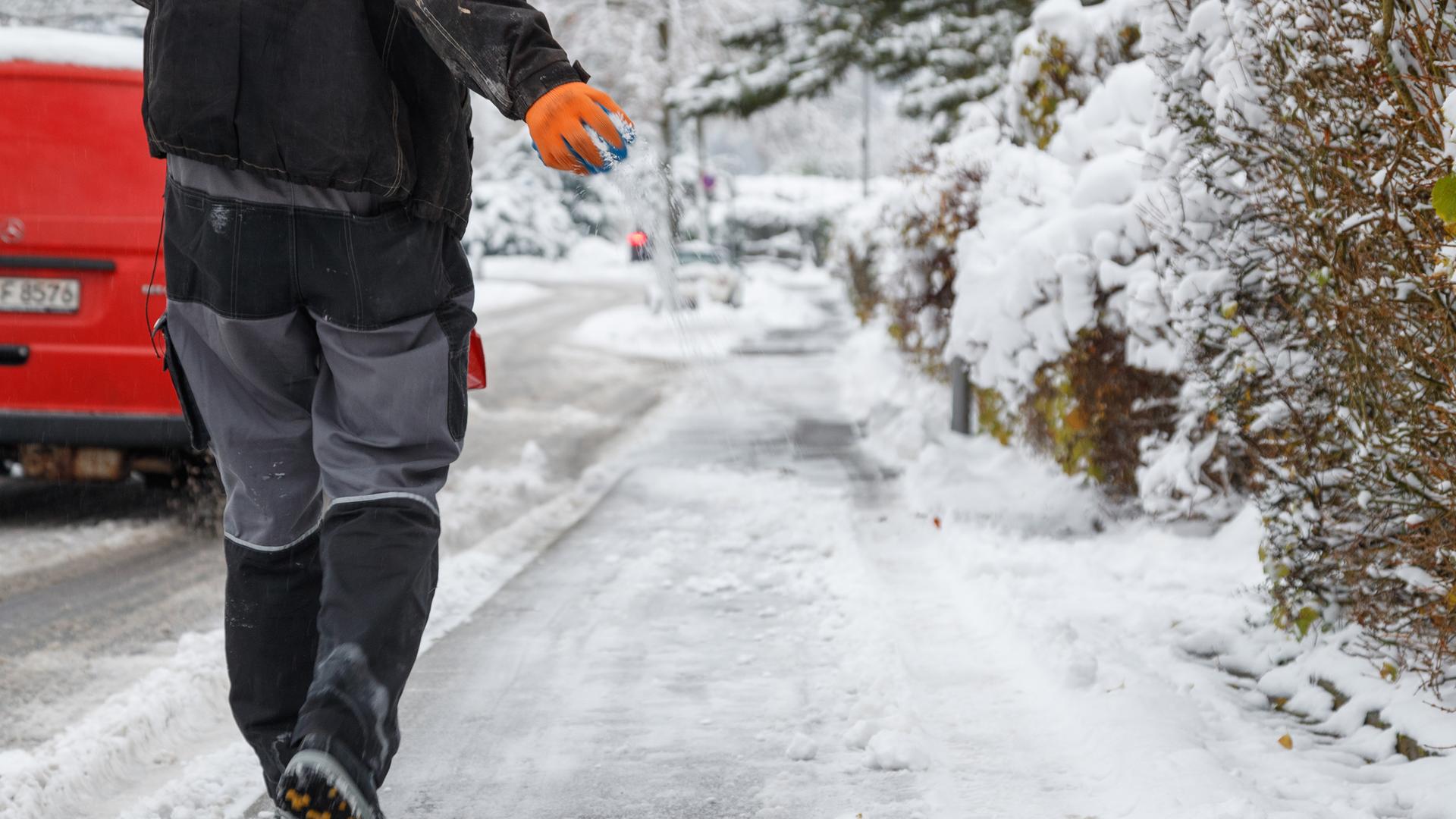 Ein Mitarbeiter vom Winterdienst streut Streusalz auf einen Gehweg.