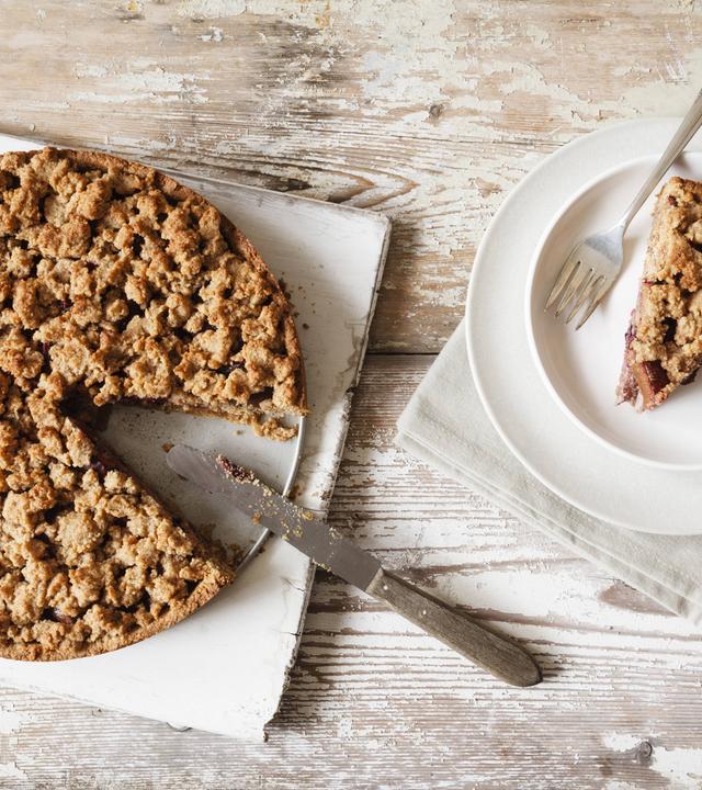 Ein Brett mit Streuselkuchen und Messer, rechts daneben ein Teller mit einem Stück Streuselkuchen mit einer Gabel.