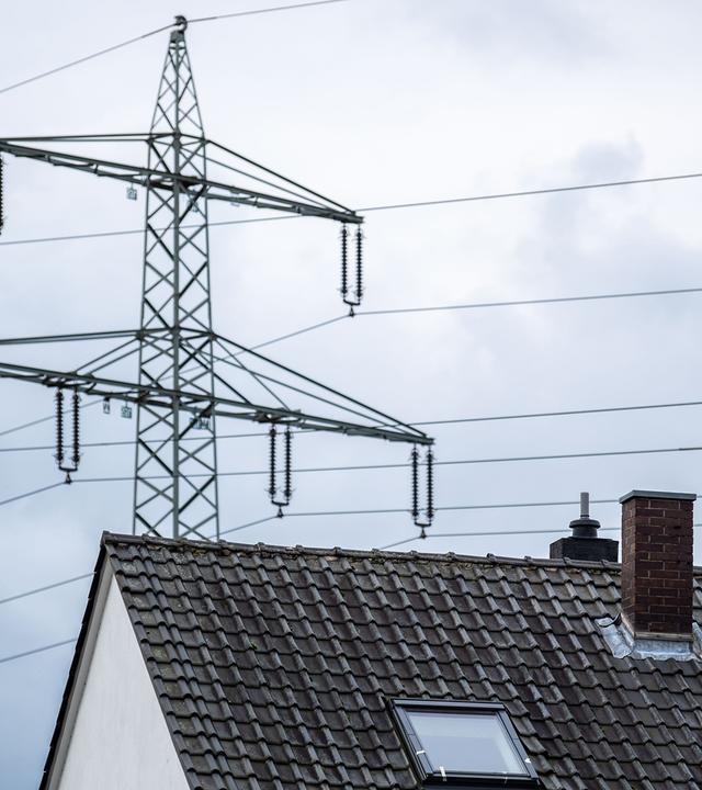 Ein Strommast steht hinter einem Wohnhaus.