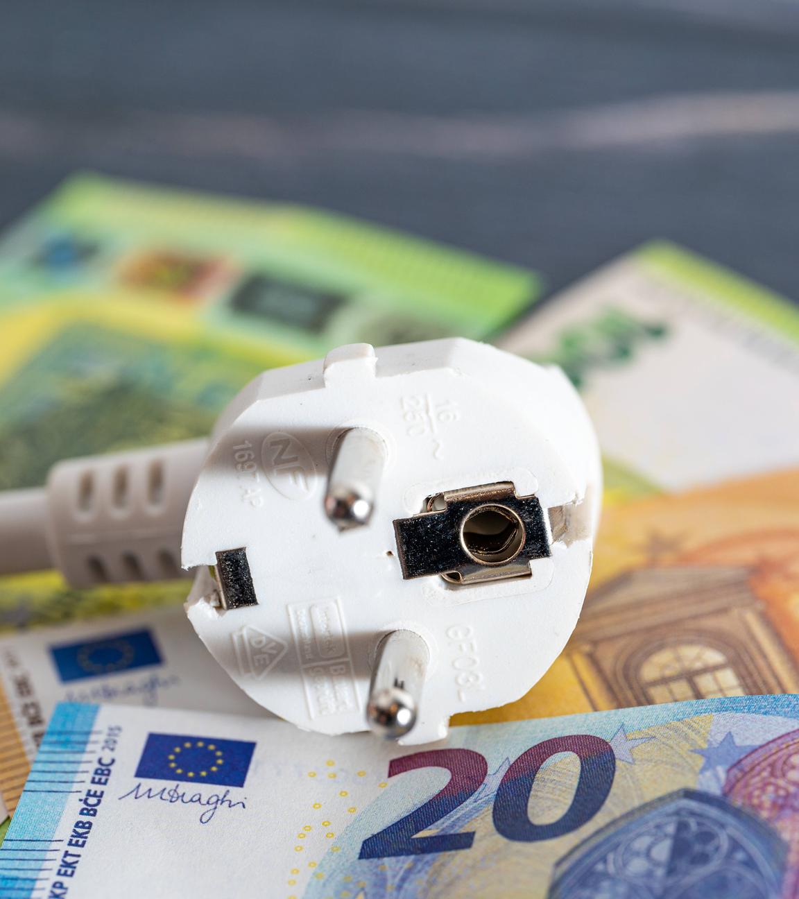 Ein Stromkabel-Stecker liegt auf Euroscheinen.