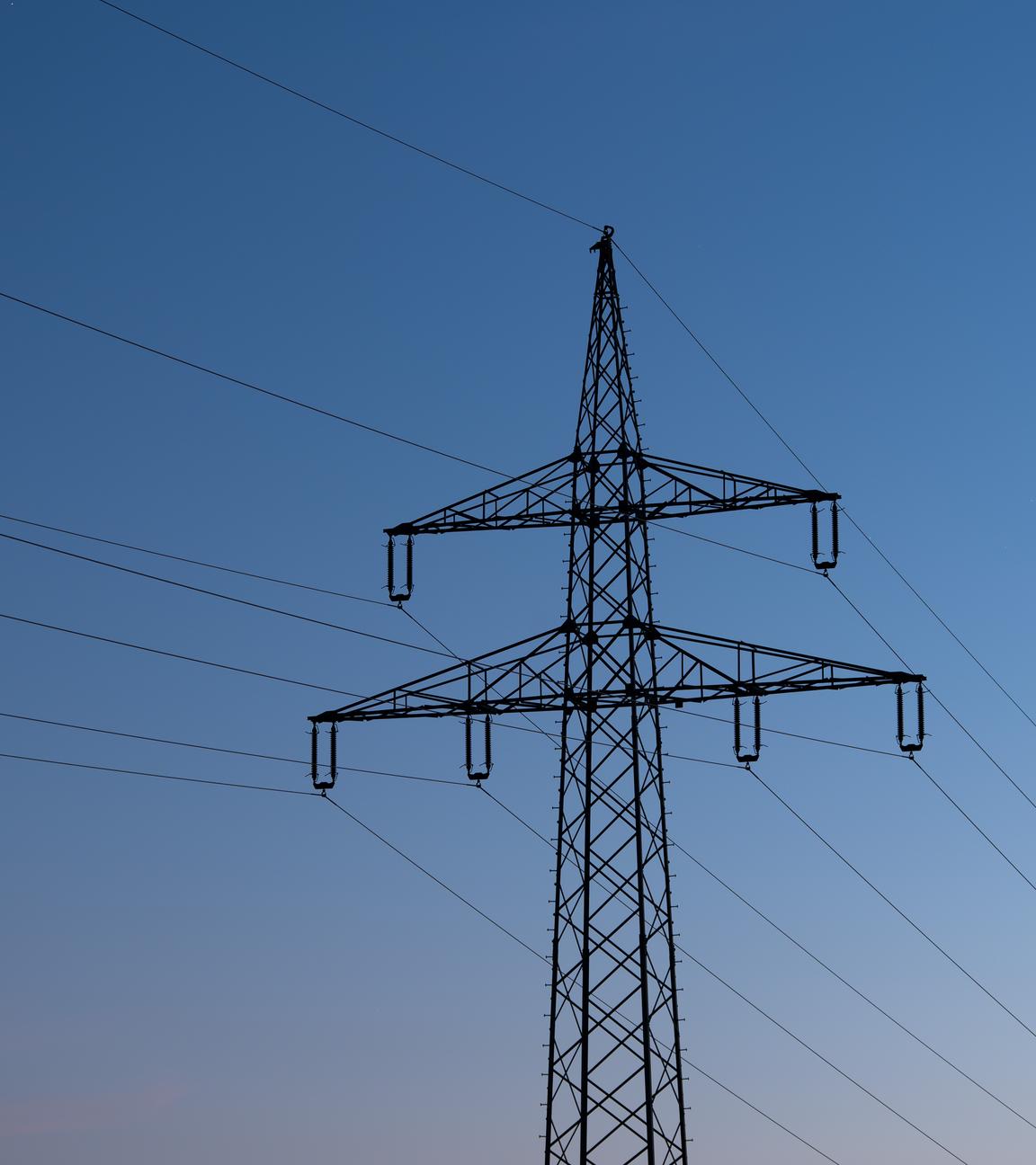 Ein Strommast ist bei Sonnenaufgang als Silhouette zu sehen.