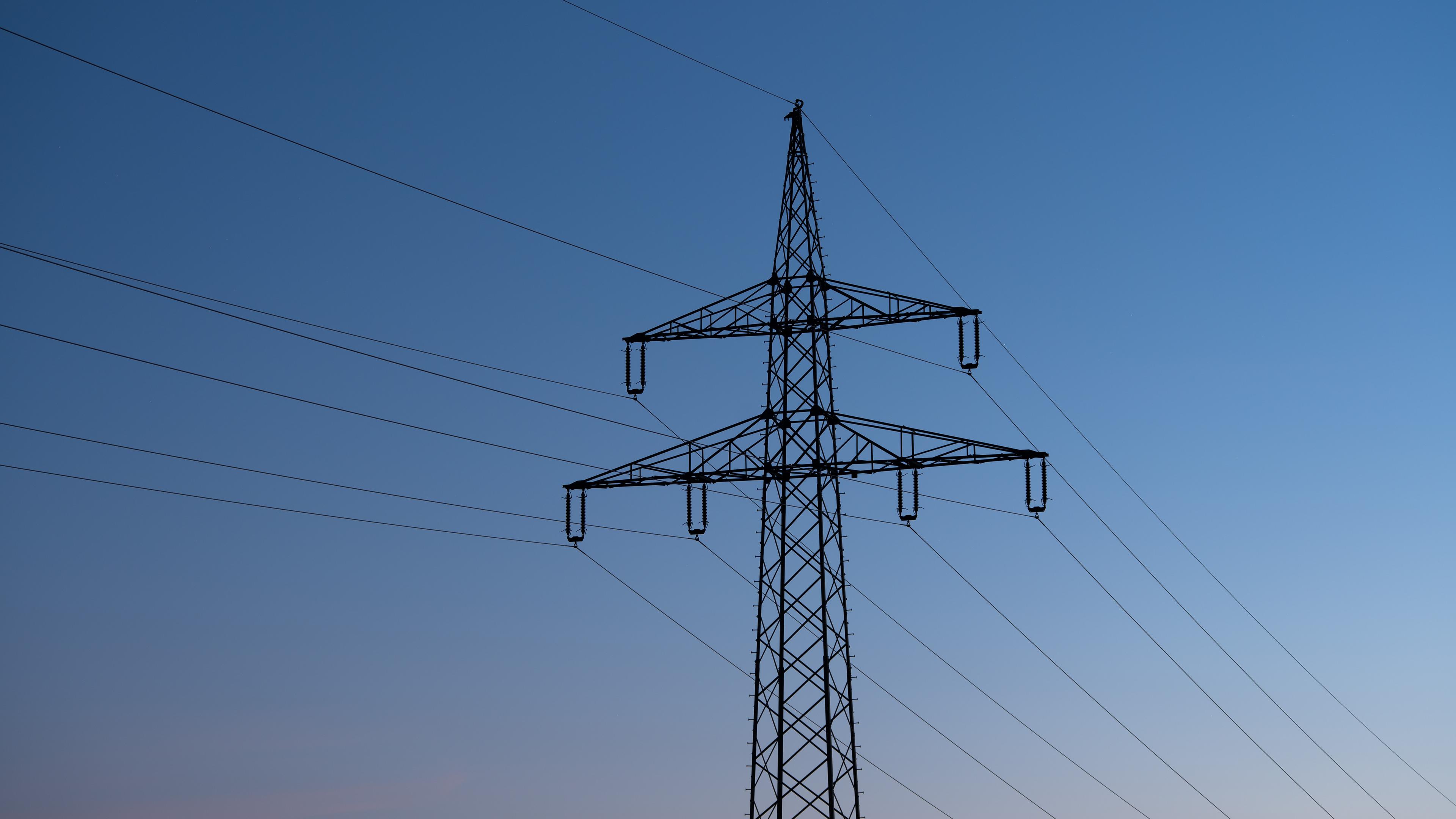 Ein Strommast ist bei Sonnenaufgang als Silhouette zu sehen.