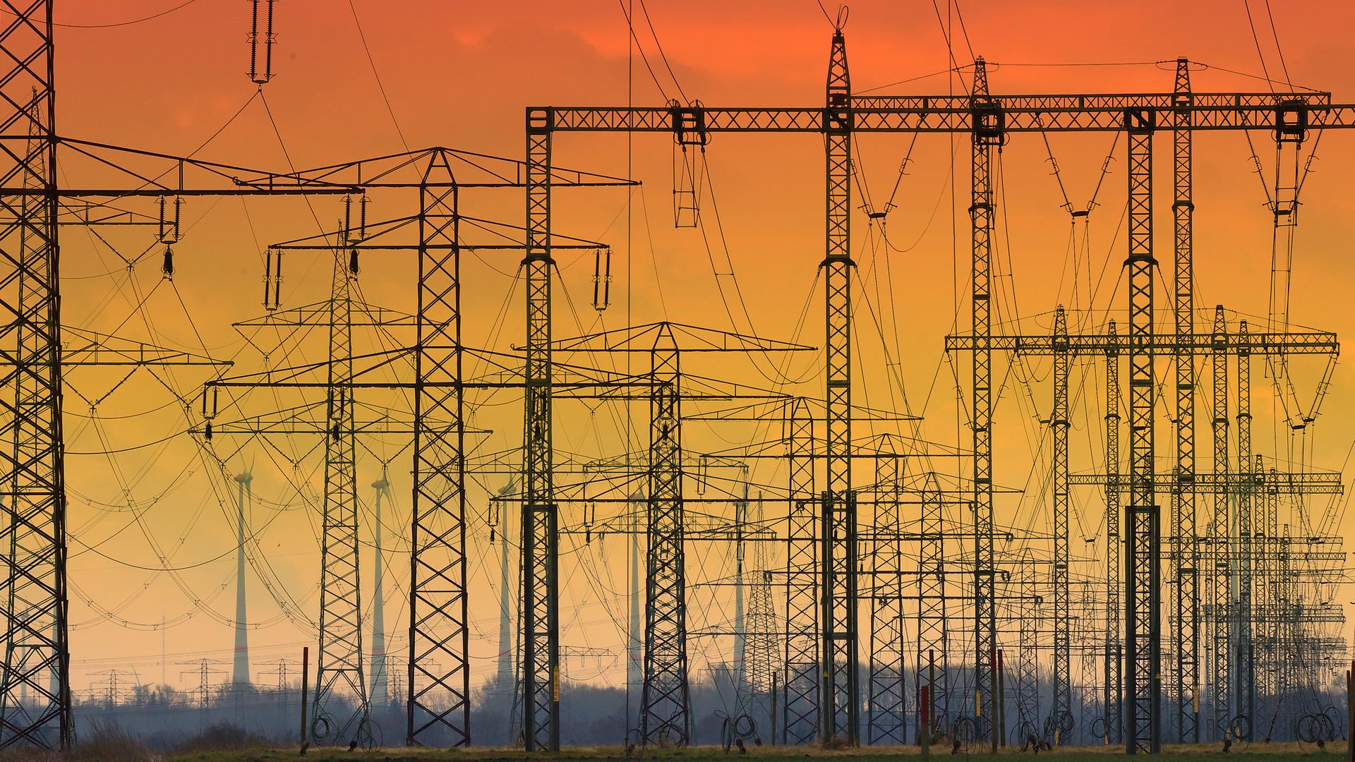 Die untergehende Sonne hat den Himmel hinter Hochspannungsleitungen verfärbt. 