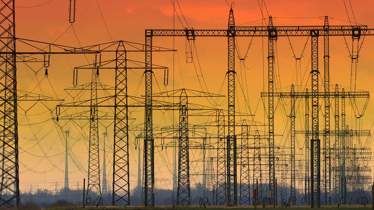 Die untergehende Sonne hat den Himmel hinter Hochspannungsleitungen verfärbt. 