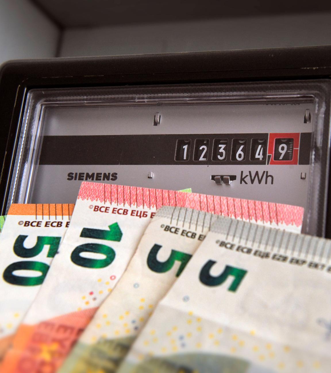 Symbolfoto: Ein Stromzähler mit Kilowattstundenzähler und verschiedenen Geldscheinen davor