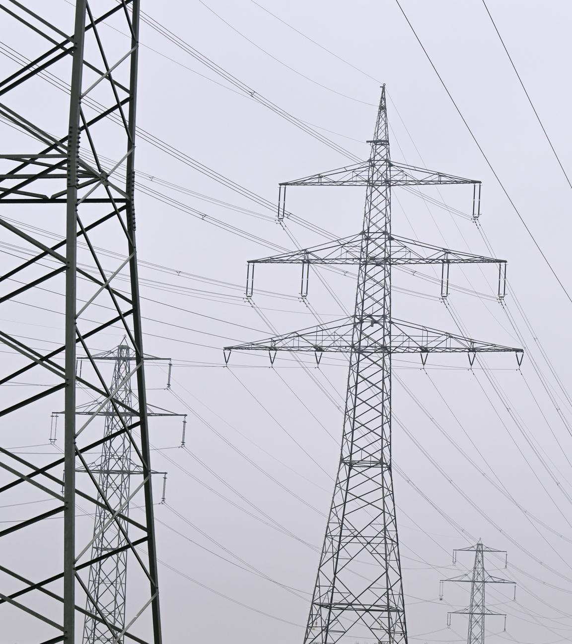Mehrere Strommasten von Überlandleitungen stehen in der Nähe eines Umspannwerks.