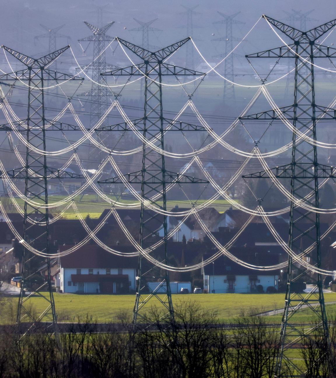 Stromleitungen an Hochspannungsmasten leuchten im Gegenlicht der Sonne.