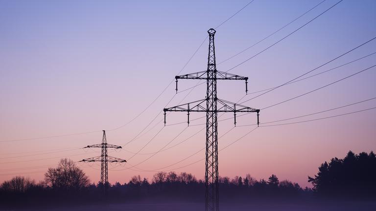 Nebel zieht über ein Solarfeld mit darüber laufender Stromleitungen.