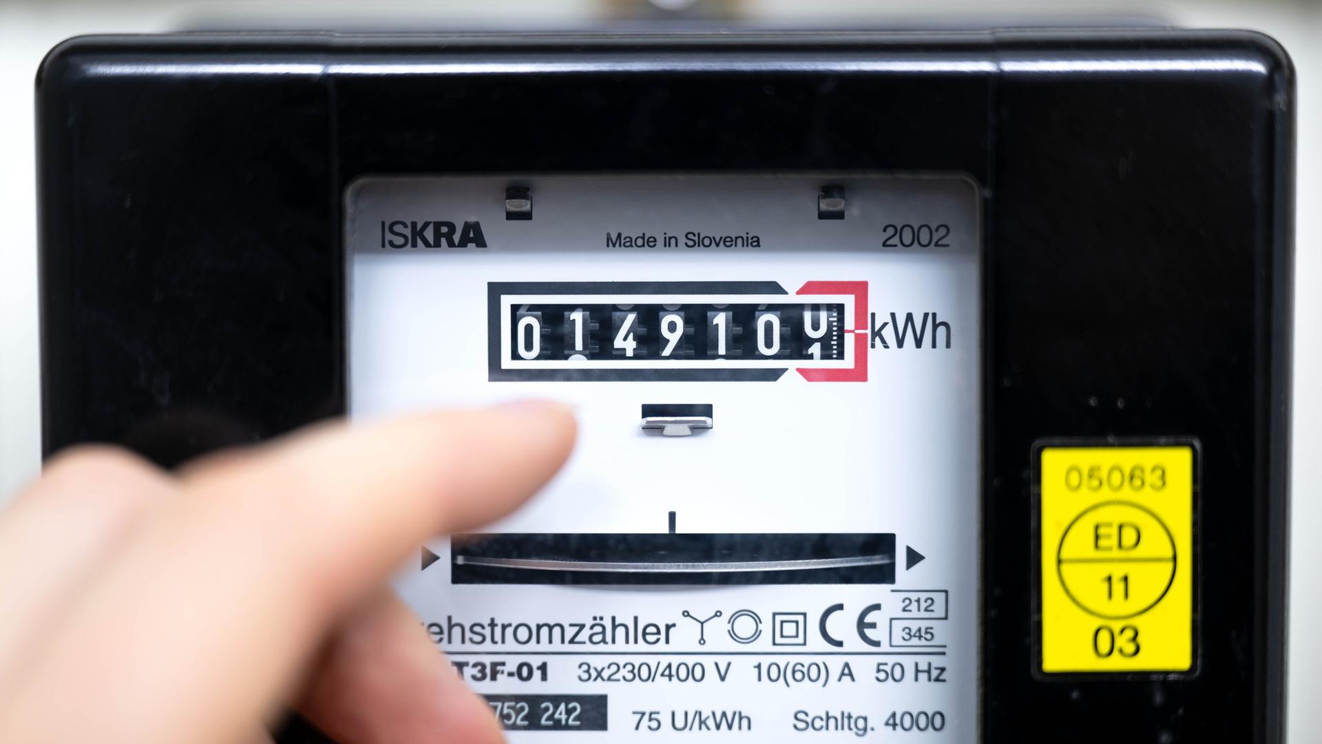 Jemand zeigt mit den Fingern auf die Anzeige eines Stromzählers