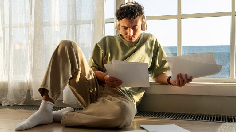 Ein Student sitzt auf dem Boden und schaut sich Dokumente an