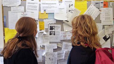 Marlene von Tronchen studieren Aushänge am schwarzen Brett der Berliner Humboldt-Universität