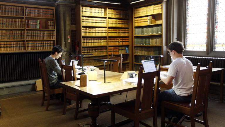 Zwei Studenten sitzen in der Universitätsbibliothek in Oxford an ihren Laptops.