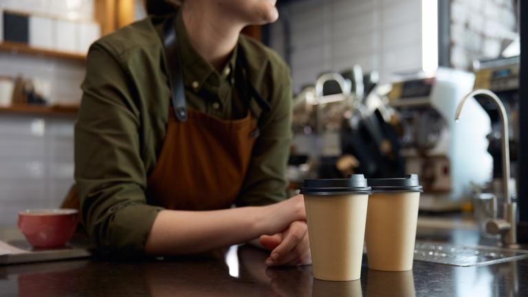 Eine weibliche Barista mit zwei Bechern Coffee to go.