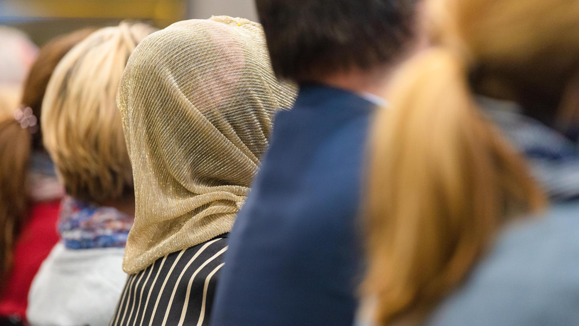 Mehrere Personen von hinten, sitzend in einer Reihe, unter ihnen eine Kopftuchträgerin