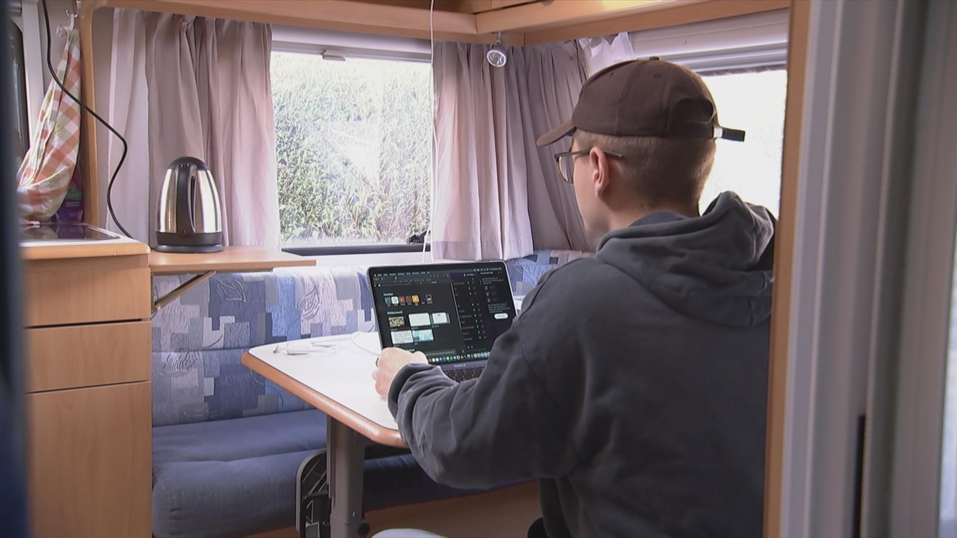 Student sitzt mit seinem Laptop am Tisch in einem Wohnmobil.