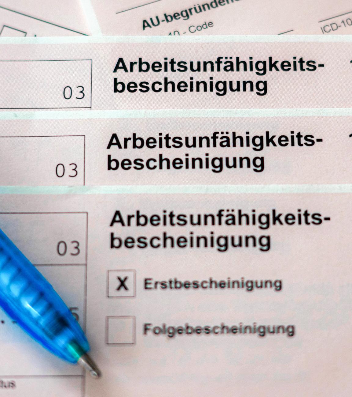 ILLUSTRATION - 18.02.2026, Bremen: Mehrere Exemplare einer Arbeitsunfähigkeitsbescheinigung liegen übereinander, daneben ein Kugelschreiber.