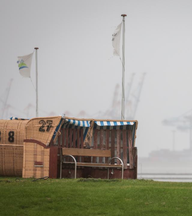 04.10.2025, Niedersachsen, Wremen: Leere Strandkörbe stehen unter einem grauen, regnerischen Himmel am Kutterhafen von Wremen.