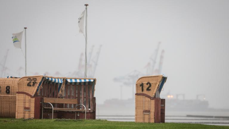 04.10.2025, Niedersachsen, Wremen: Leere Strandkörbe stehen unter einem grauen, regnerischen Himmel am Kutterhafen von Wremen.