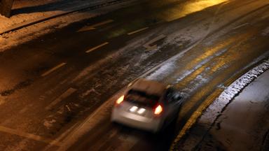 Bayern, Würzburg: Ein Auto fährt am frühen Morgen auf einer teilweise mit Schnee bedeckten Straße.
