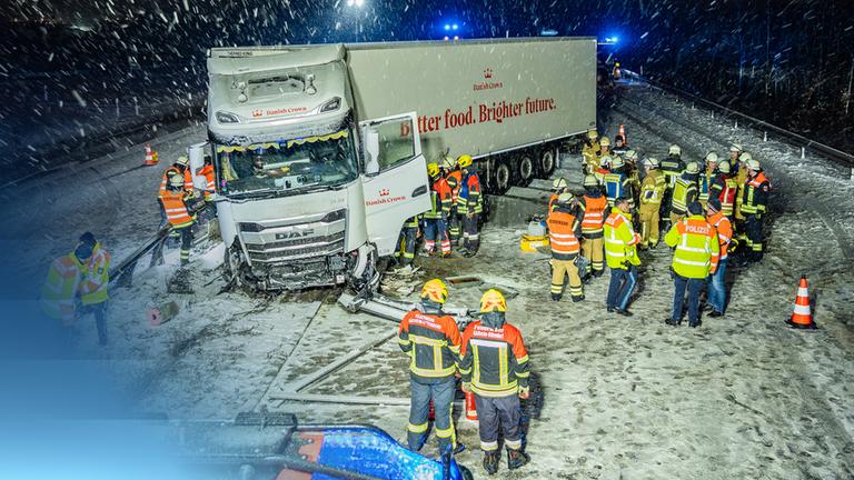 Ein demolierter LKW im Schnee auf einer Autobahn von Einsatzkräften umgeben