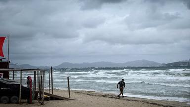 Ein Spaziergänger geht bei stürmischem Wetter und hohem Seegang am Strand von Mallorca entlang. Am Rettungsturm weht die rote Flagge (absolutes Badeverbot) aufgrund von starkem Wind, hohem Wellengang und Unwettergefahr. 