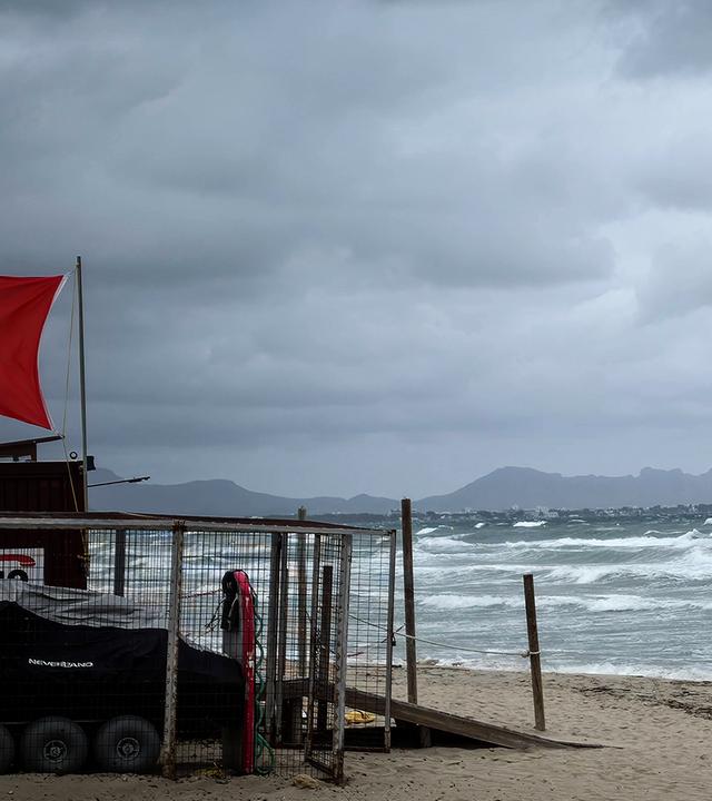 Ein Spaziergänger geht bei stürmischem Wetter und hohem Seegang am Strand von Mallorca entlang. Am Rettungsturm weht die rote Flagge (absolutes Badeverbot) aufgrund von starkem Wind, hohem Wellengang und Unwettergefahr. 