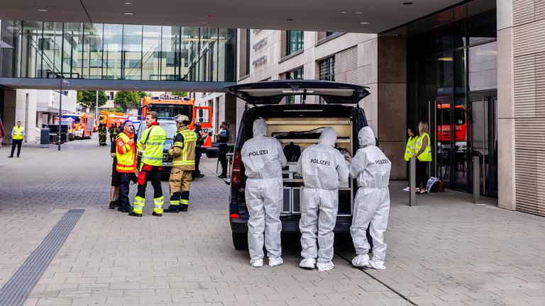 Beamte der Spurensicherung stehen bei einem größeren Polizeieinsatz vor einem Einkaufszentrum in der Innenstadt.