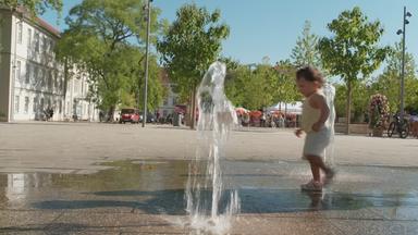 Ein kleines Kind läuft durch einen Springbrunnen in der Stadt.
