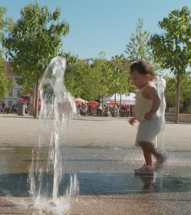 Ein kleines Kind läuft durch einen Springbrunnen in der Stadt.