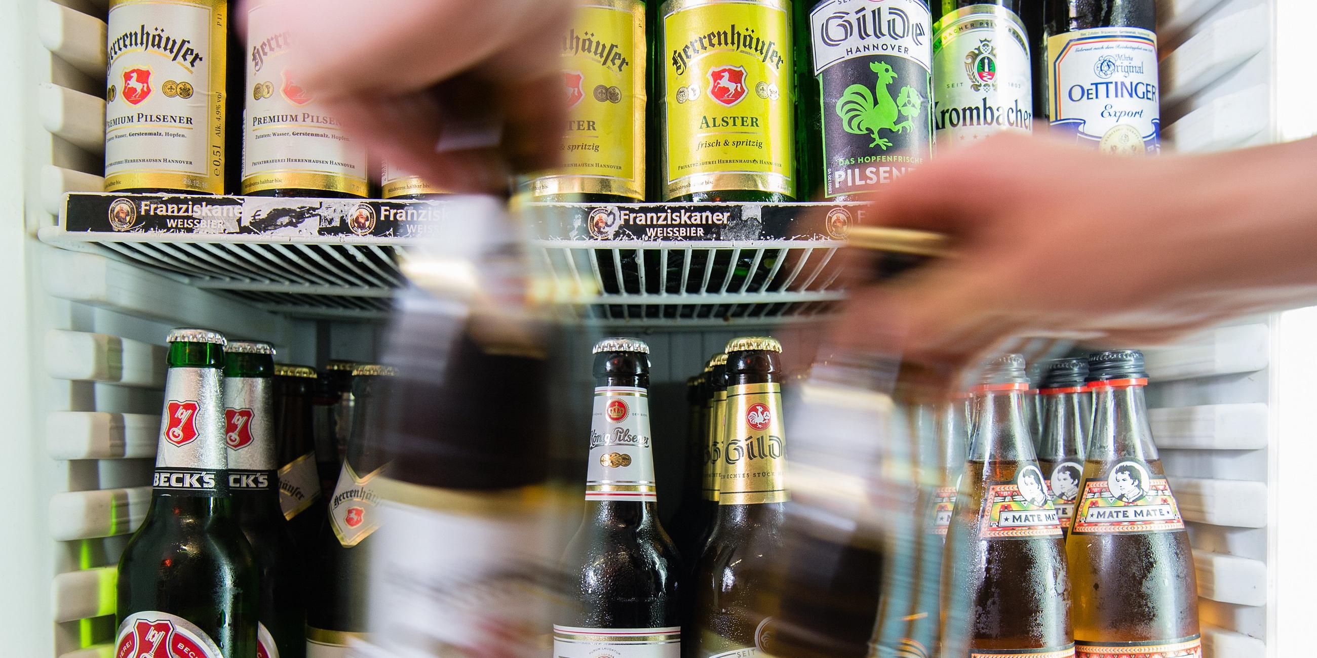Symbolfoto: Ein mann  nimmt zwei flaschen Bier aus einem Kühlschrank.