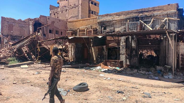 Ein bewaffneter Kämpfer patrouilliert in einem Marktgebiet in Khartum, während der Krieg im Sudan zwischen Armee und RSF große Zerstörung und humanitäre Krise verursacht.