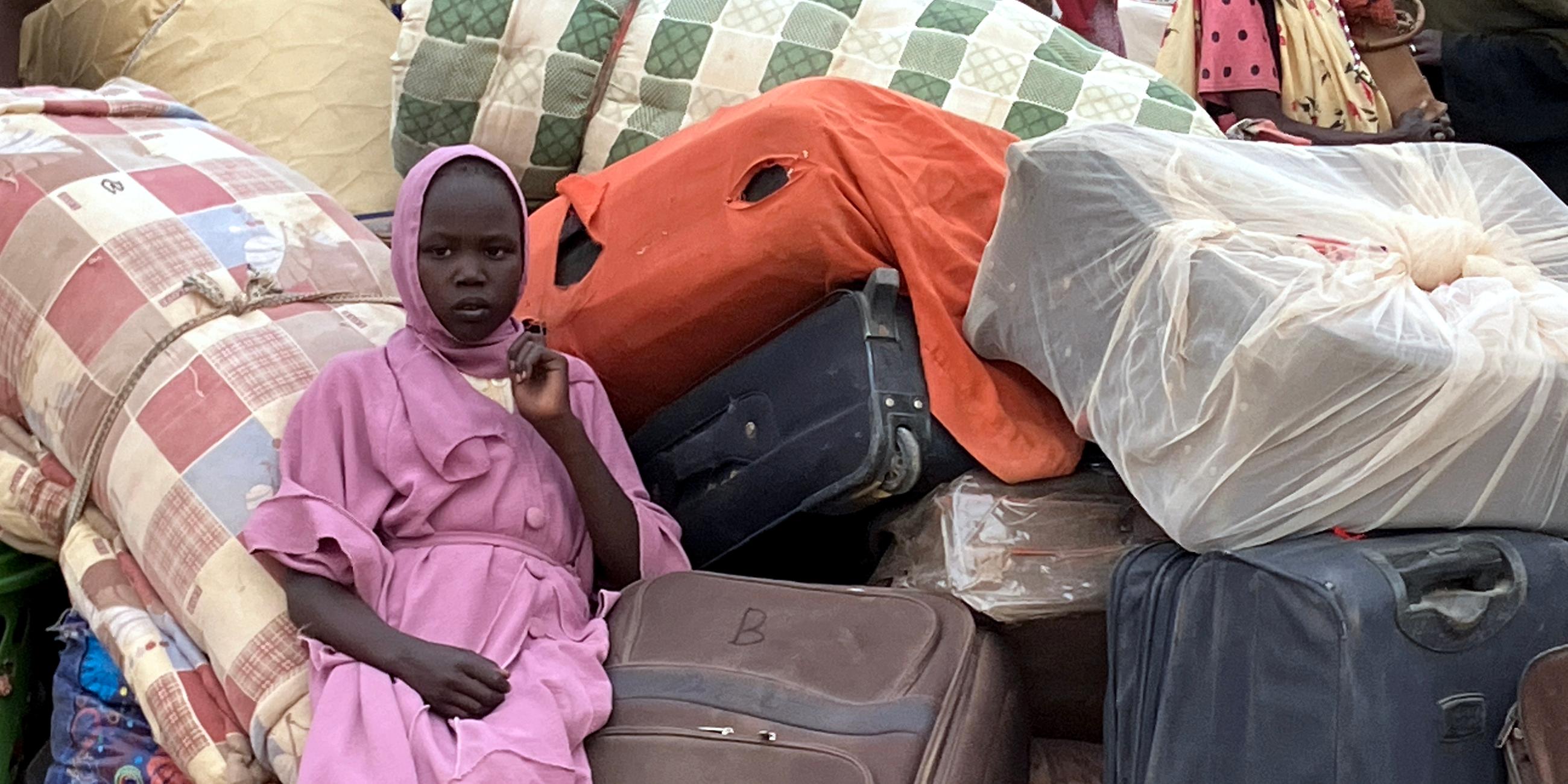 Eine junge Frau aus dem Sudan sitzt in einem Flüchtlingslager inmitten von Koffern
