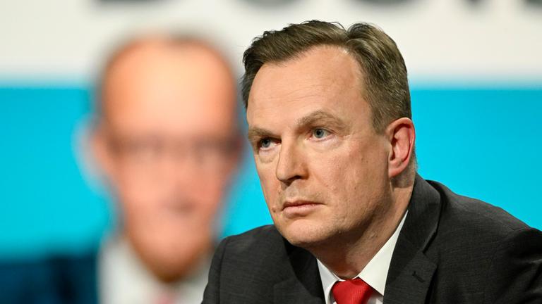 Jens Südekum in der Sendung "Markus Lanz", im Hintergrund ein verschwommenes Bild von Friedrich Merz