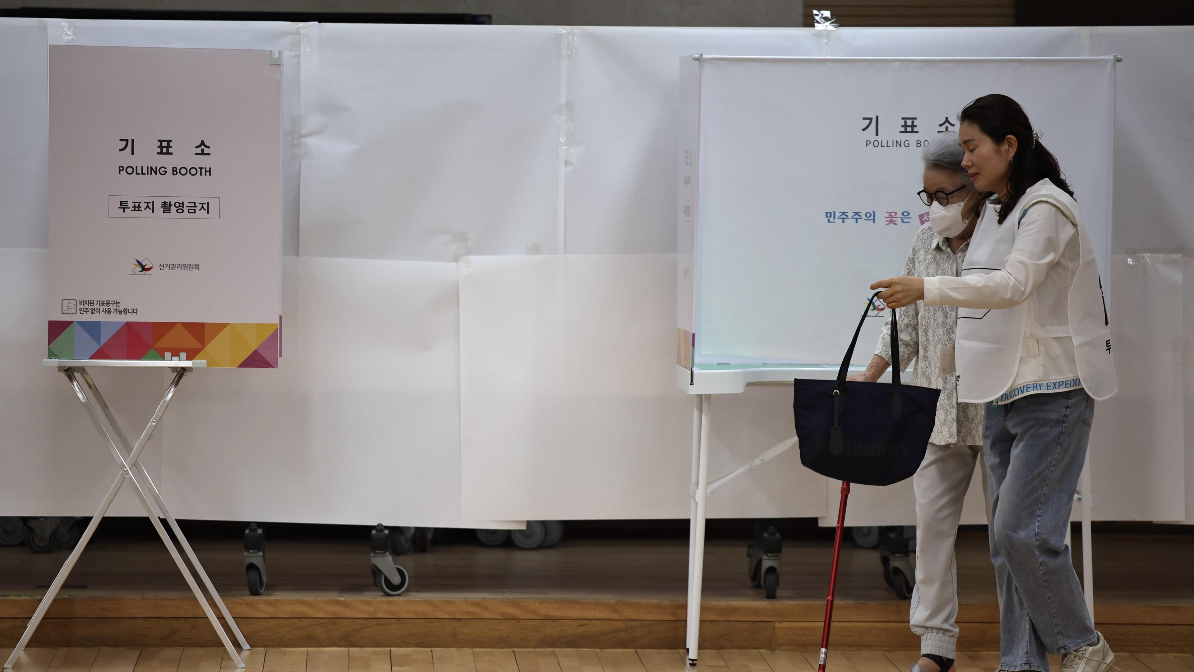 Eine Frau hilft einer älteren Frau in die Wahlkabine.