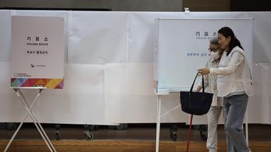 Eine Frau hilft einer älteren Frau in die Wahlkabine.
