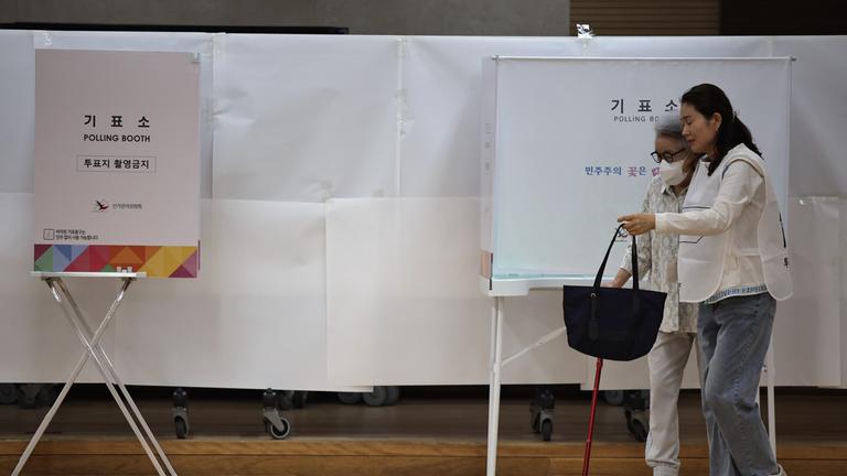 Eine Frau hilft einer älteren Frau in die Wahlkabine.