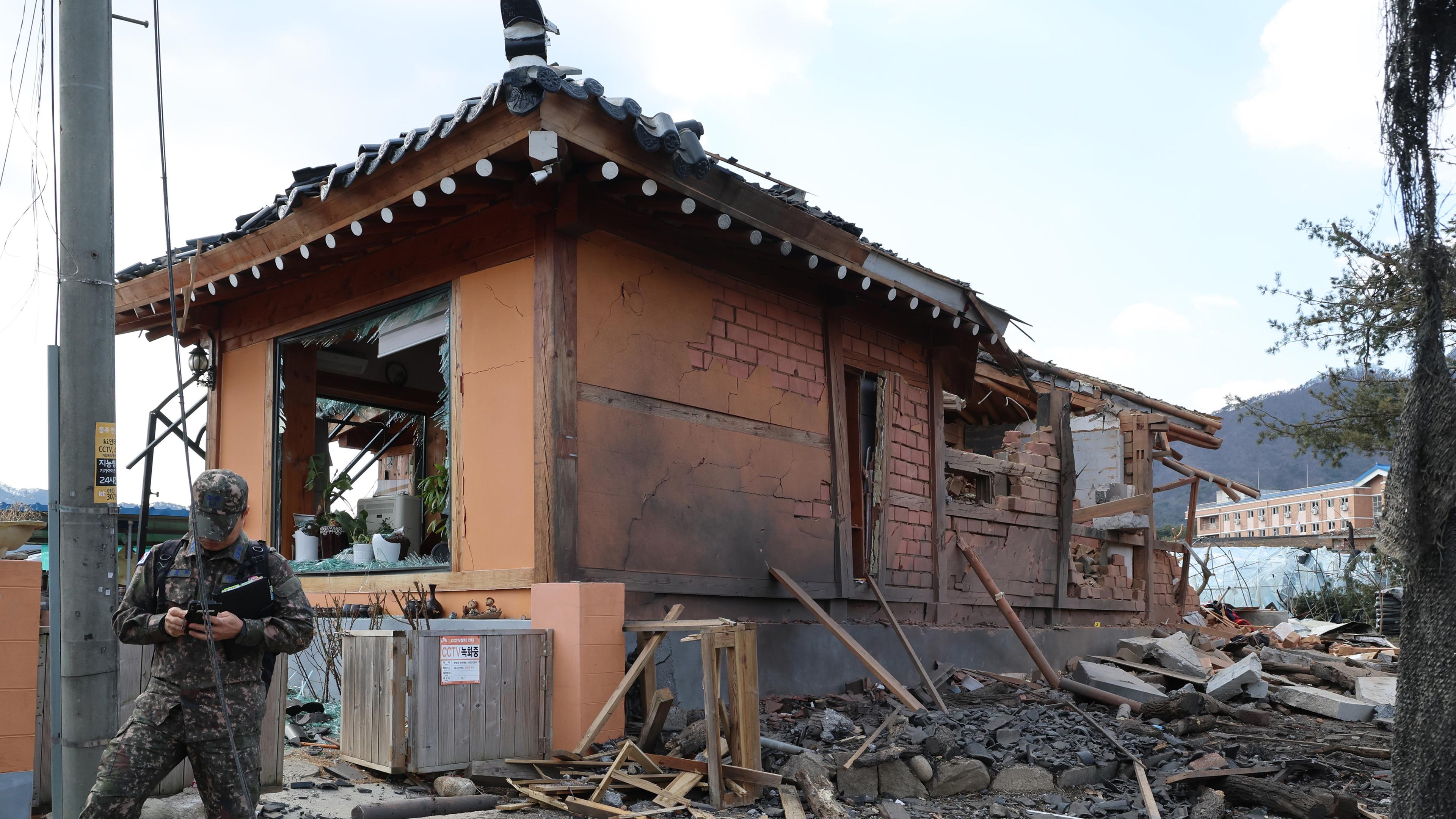 Ein Soldat steht vor einem Haus in Trümmern. Das Haus wurde bei einem versehentlichen Kampfjet-Bombenabwurf auf ziviles Gebiet beschädigt. 