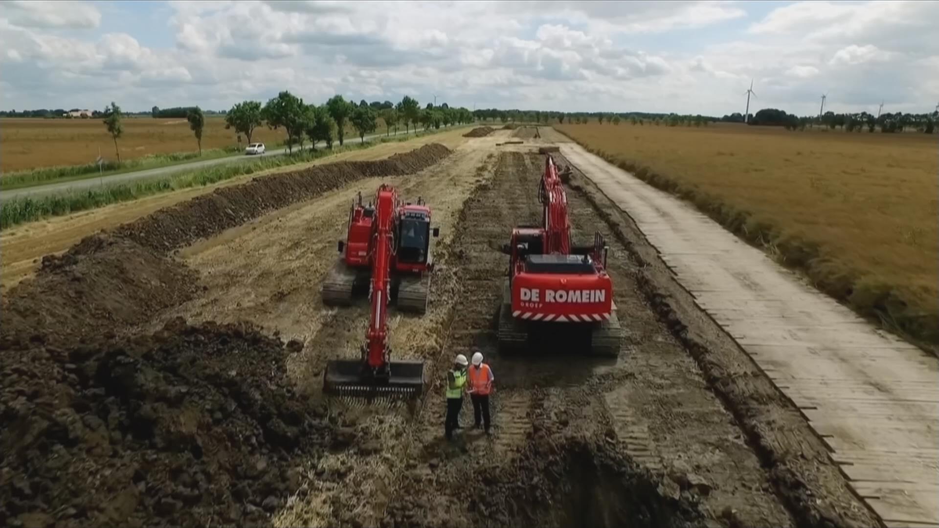 Zwei Bagger stehen auf Baustelle der SüdLink-Trasse neben Feldern in Schleswig-Holstein, davor zwei Männer mit Bauarbeiterhelmen und Warnwesten