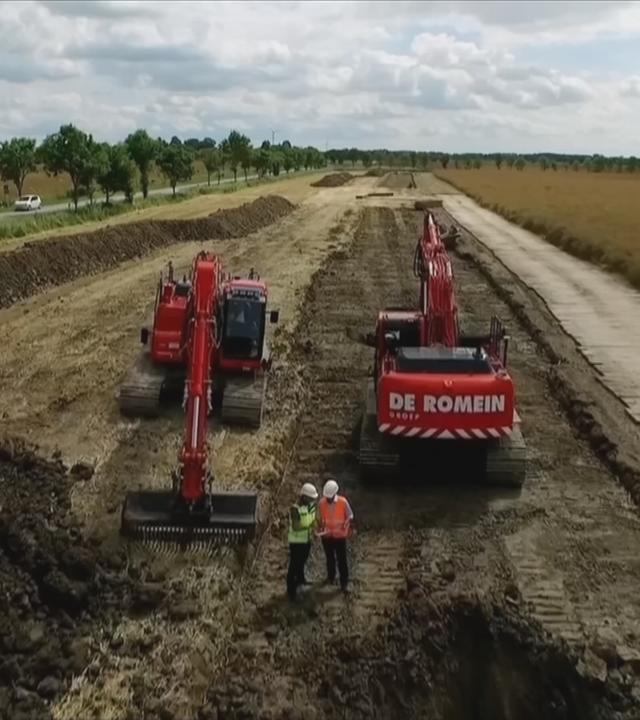 Zwei Bagger stehen auf Baustelle der SüdLink-Trasse neben Feldern in Schleswig-Holstein, davor zwei Männer mit Bauarbeiterhelmen und Warnwesten
