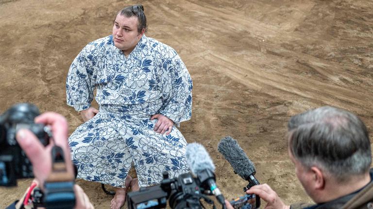 Der ukrainische Sumo-Ringer Aonishiki. Er sitzt und wird von Paperazzis fotografiert.