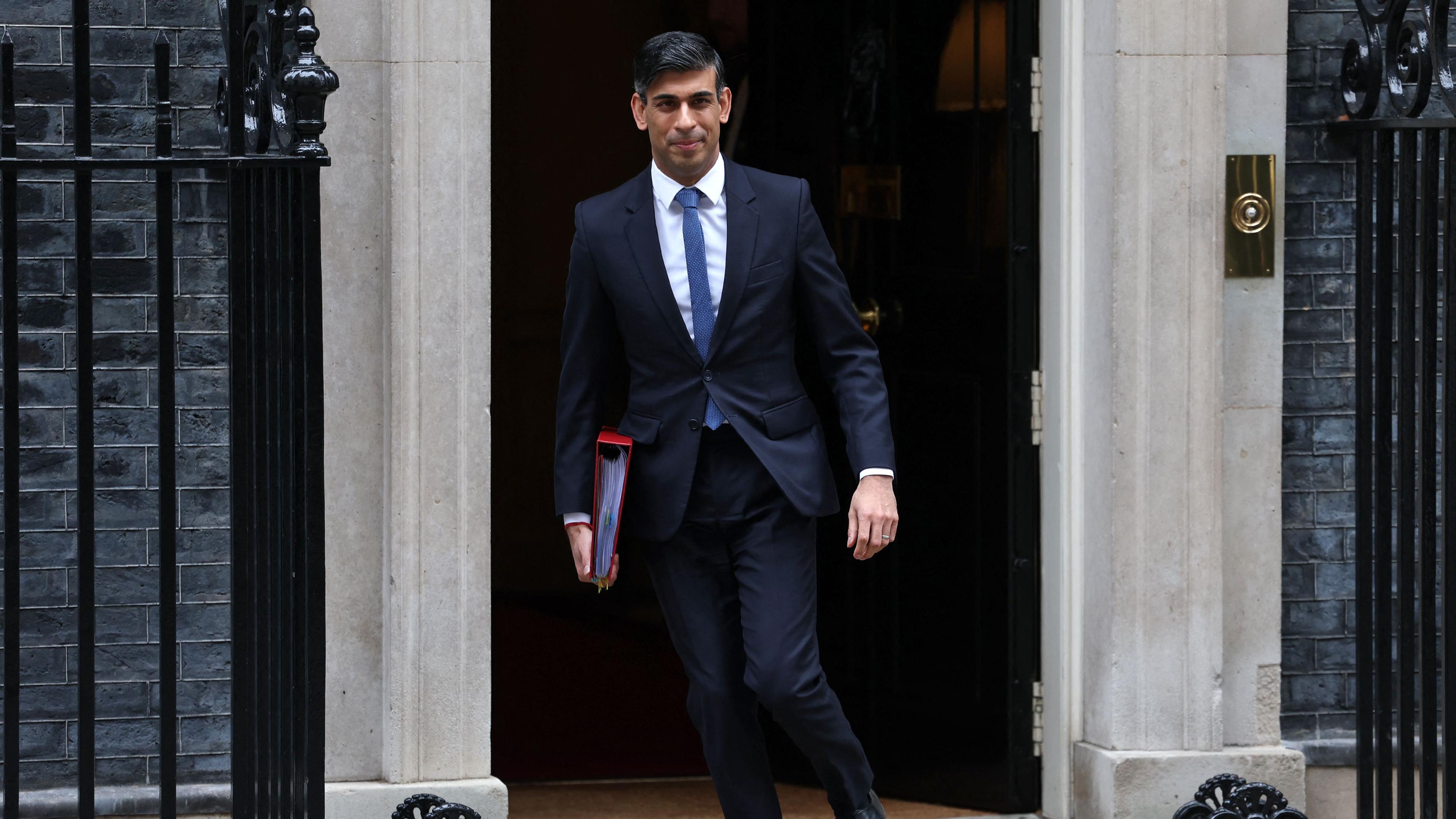 Rishi Sunak geht mit Akten in der Hand.