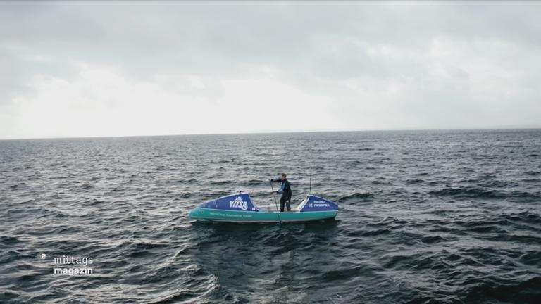 Ein Mann steht auf einem Stand-Up-Paddleboard, um ihn herum nur Meer