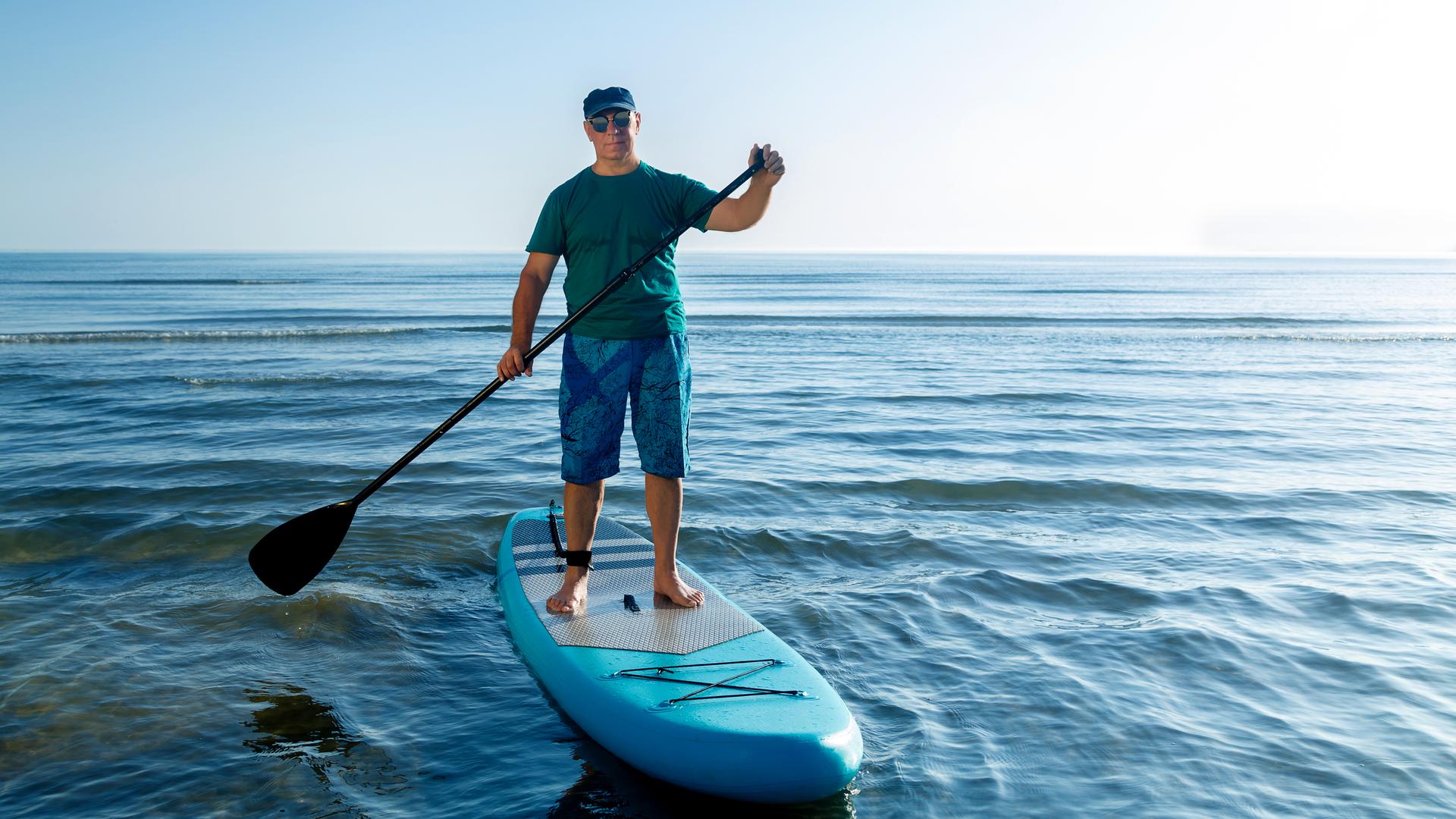 En Mann steht auf einem SUP und hält ein Paddel in der Hand.