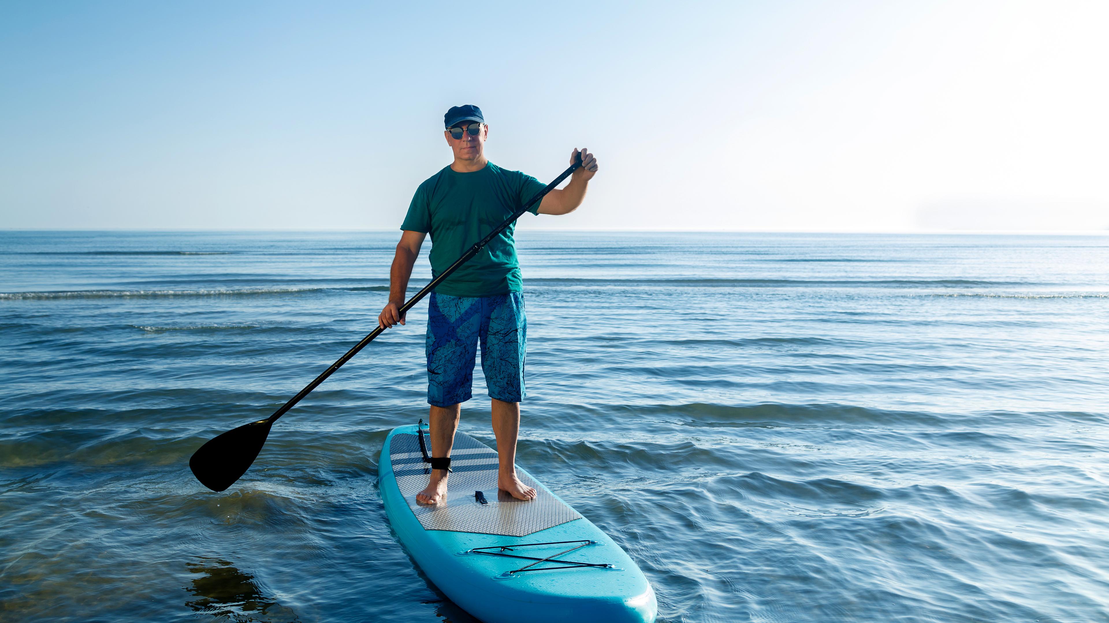 En Mann steht auf einem SUP und hält ein Paddel in der Hand.