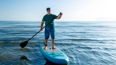 En Mann steht auf einem SUP und hält ein Paddel in der Hand.