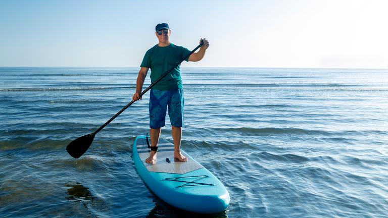 En Mann steht auf einem SUP und hält ein Paddel in der Hand.
