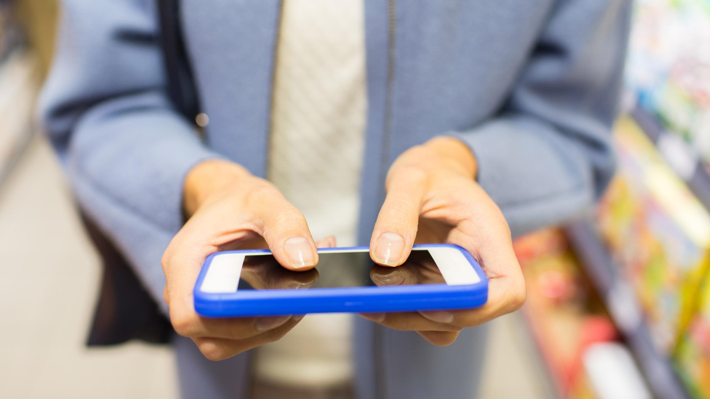 Frau tippt auf Smartphone in einem Supermarkt.