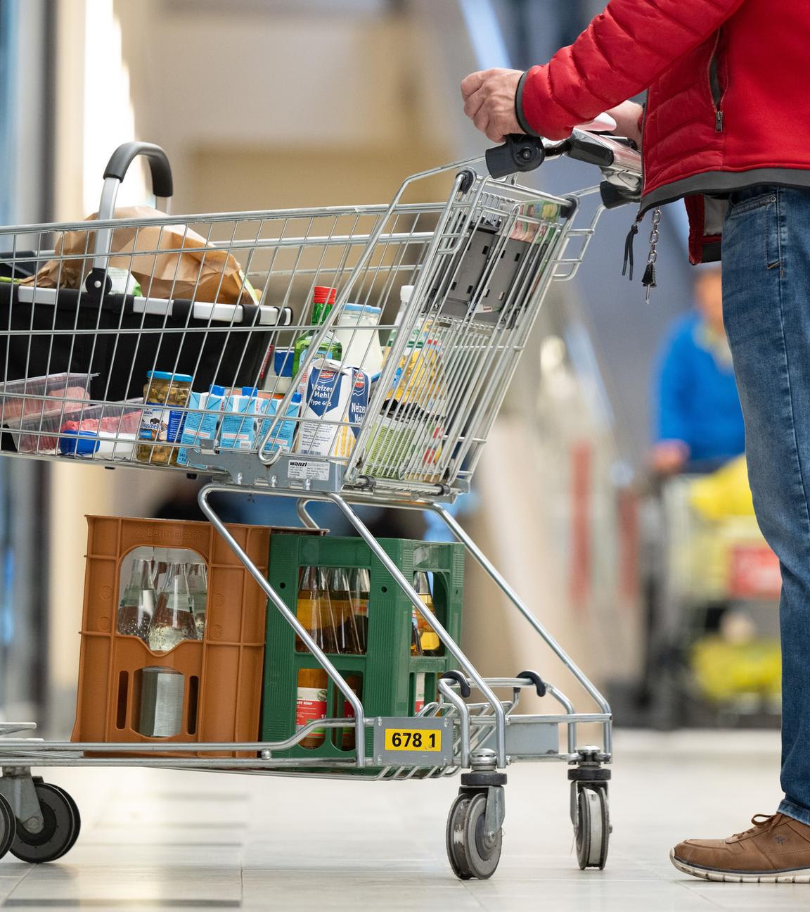 Ein Mann steht vor einem Supermarkt mit einem vollen Einkaufskorb.
