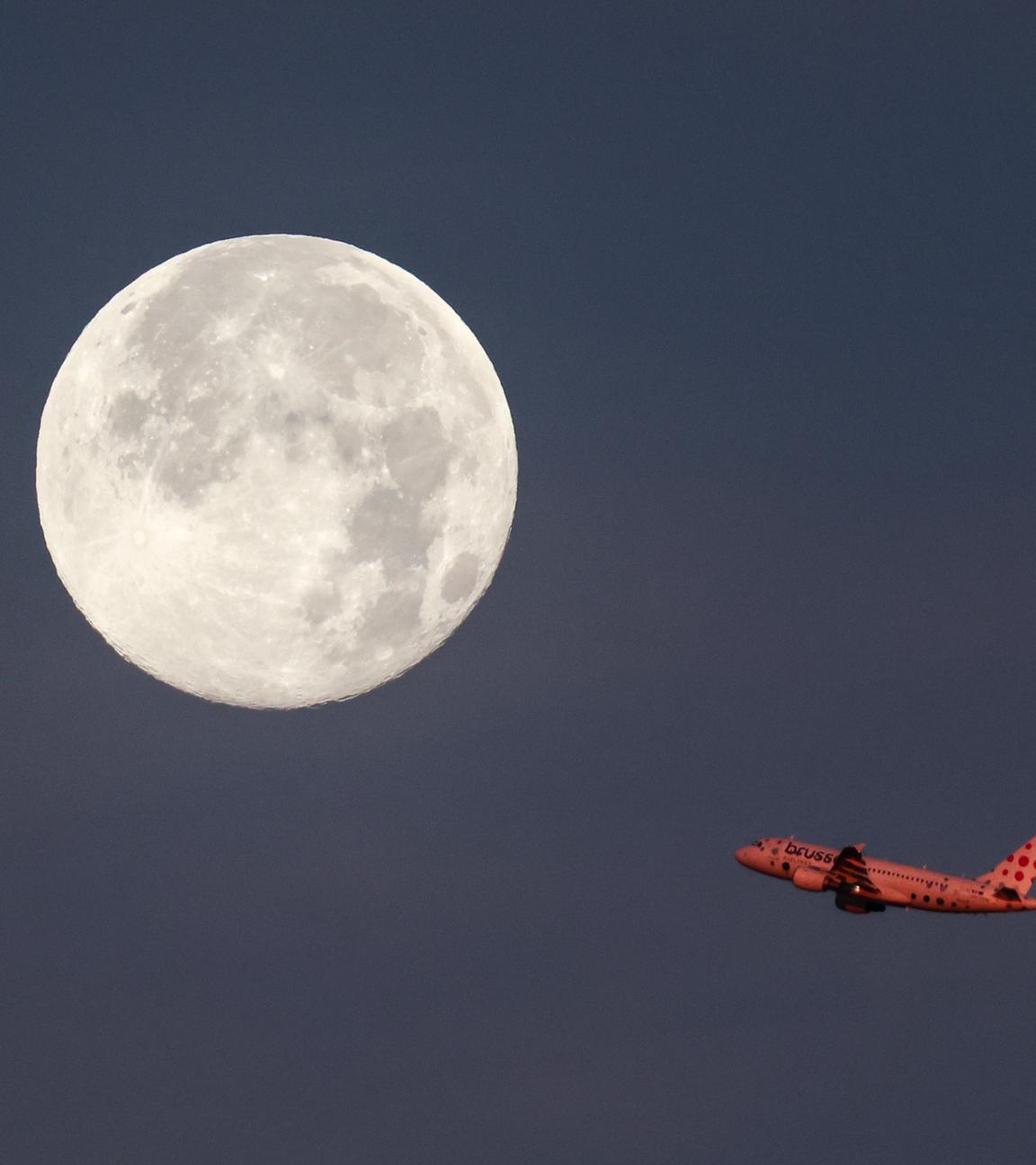 Ein Passagierflugzeug startet vom Airport in Hamburg und fliegt vor dem untergehenden Mond vorbei. 